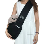 Woman wearing black sling carrier with plush dog demonstrating front pocket and wide strap